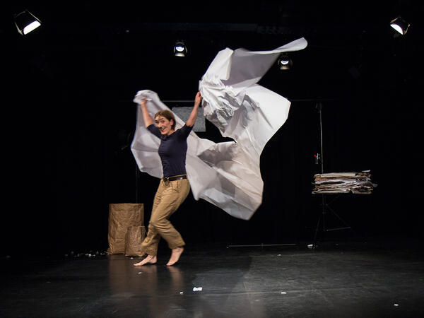 Eine Frau rennt mit einem großen Bogen Papier über eine Bühne.