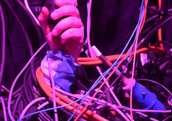Neonfarbenes Licht, eine Hand in einem Netz aus Kabeln.