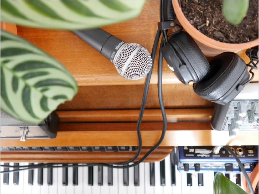 Bild vergrößern: Ein Mikrophon und Köpfhörer liegen auf einem Klavier. Ein Stück einer Pflanze ist auch zu sehen. Das Bild wirkt hell und einladend.